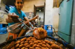 කොළ පාට ටී ෂර්ට් එකක් සහ මල් වැටුණු සායක් ඇඳ සිටින කාන්තාවක් කැවුම් බඳින ආකාරය පෙනේ.