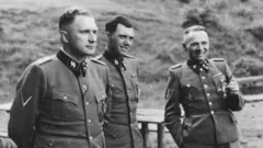 Três homens com uniforme nazista da SS em uma foto em preto e branco