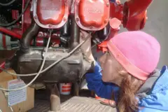 Sabrina González Pasterski, usando um gorro rosa e uma jaqueta azul, e vendo peças de um avião.