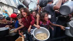 Niños con recipientes luchan entre una multitud por recibir comida