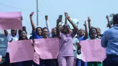 Foto of health workers wey carry placards dey protest.