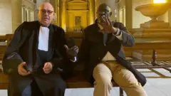 Séraphin Twahirwa (i buryo) ari kumwe n'uwumwunganira Maître Jean Flamme