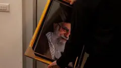 یک مرد که از پشت سر دیده‌می شود قاب عکس علی خامنه‌ای را در دست دارد.