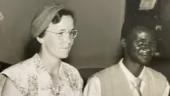 Foto antiga mostra os noivos no casamento; eles sorriem contidamente 