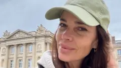 Mulher tirando selfie, com sorriso contido, em frente a construção histórica