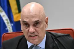 Alexandre de Moraes falando ao microfone em audiência, com bandeira do Brasil atrás