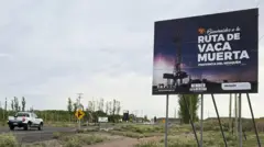 Estrada por onde passa uma caminhonete, com um cartaz dando as boas-vindas a Vaca Muerta