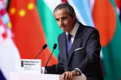 Rafael Grossi en un podio frente a un micrófono y en el fondo se ven varias banderas