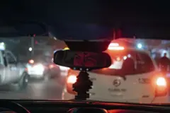 Um homem dirigindo um carro. A imagem dele é vista pelo retrovisor