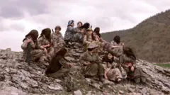 Des combattantes du PJAK, armes à la main, sont assises au sommet d'une colline rocheuse. Certaines portent un voile couvrant leur tête et leur visage, et beaucoup sont armées.