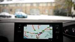 Спутниковый навигатор в машине на фоне заснеженного пейзажа.