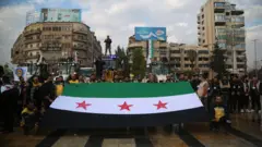 أعضاء من فريق الدفاع المدني السوري، الخوذ البيضاء، ومتطوعون آخرون يحملون علم سوريا الجديد خلال تجمع للإعلان عن بدء حملة إصلاح في حلب.