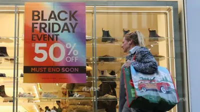 Woman walking past shop window with 'Black Friday 50% off' sign