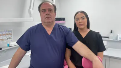 A man and and a younger woman is scrubs, stand in a dental surgery room looking dejected