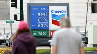 ガソリンスタンドに表示されている価格を、歩道から男女が見ている