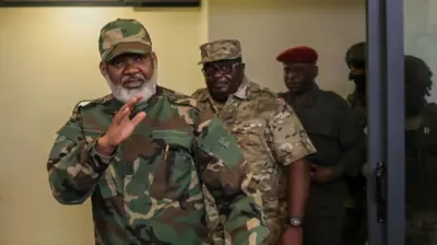 Umuhuzabikorwa wa AFC/M23 Corneille Nangaa n'umwungirije akaba n'umukuru wa M23, Bertrand Bisimwa, barimo kugenda binjira mu cyumba, inyuma yabo hari inyeshyamba z'uwo mutwe zibacungiye umutekano. Nangaa akoze ikimenyetso n'ikiganza asuhuza ndetse we na Bisimwa bambaye imyenda yijimye ya gisirikare. Ifoto yo ku itariki ya 30 Mutarama (1) mu 2025, ubwo bari baje mu kiganiro n'abanyamakuru i Goma, mu burasirazuba bwa Repubulika ya Demokarasi ya Congo. 