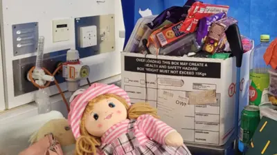 Jessie's doll and a cardboard box piled high with her possessions next to a hospital bed