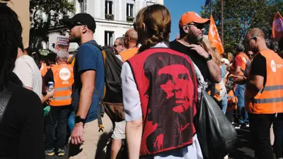Mulher de costas com um colete vermelho com a imagem de Che Guevara em preto, durante uma manifestação