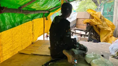 फ़ुटपाथ पर बने अस्थाई शेल्टर में बैठी एक युवती