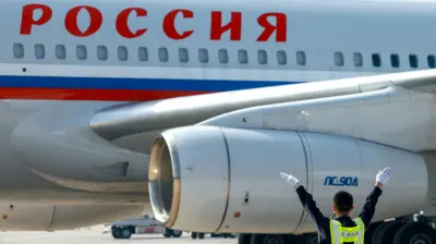 Крупным планом самолет с надписью «Россия», перед ним сотрудник аэропорта жестикулирует.