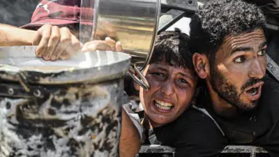 Palestinians carrying pans gather to receive hot meals from a charity kitchen in Gaza City, northern Gaza (23 July 2025)