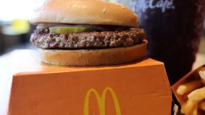 A McDonald's quarter pounder sits on an orange takeaway box with a bit of pickle and onion peeking out from under the bun