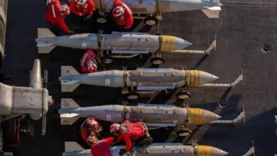 نمای بالا از ردیف موشکها و افرادی با لباس مخصوص قرمز رنگ در حال وارسی آنها