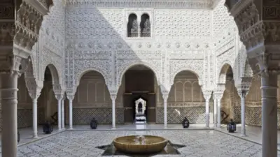 Un patio con suelo de baldosas, fuente y paredes blancas talladas con gran ornamentación.