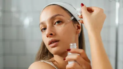 Młoda kobieta stoi w łazience i nakłada na twarz serum