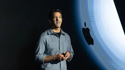 John Ternus, 4 Mart 2026'da New York'taki Apple Inc. şirketinde, mavi bir gömlek giymiş ve Apple logosunun yansıtıldığı bir arka plan önünde bir sunum yapıyor.