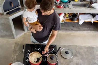 Foto de banco de imagens mostra homem cozinhando com criança no colo