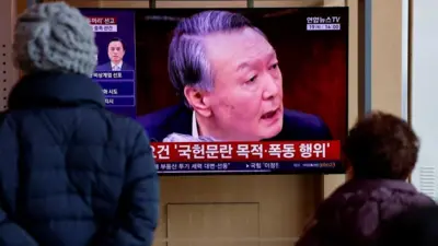 大型液晶スクリーンに尹被告の顔が大きく映っている。それをコートを着た人たちが見ている