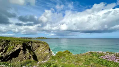 Cumulus clouds in a blue sky over a blue sea, with grass-topped cliffs in the foreground