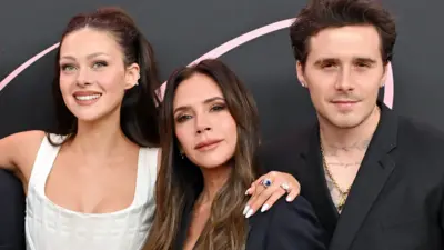  Nicola Peltz Beckham, Victoria Beckham and Brooklyn Peltz Beckham stand together at a press event . Victoria Beckham is in the middle. Nicola has her arm around Victoria. They are in evening dress