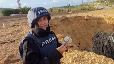 Foto da jornalista Amal Khalil, do jornal libanês Al-Akhbar, usando colete e capacete de imprensa enquanto fazia reportagem perto de uma ponte destruída em Qasmiyeh