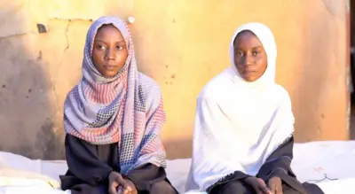 فتاتان سودانيتان ترتديان غطاء رأس (حجاباً) تجلسان بجوار بعضهما.
