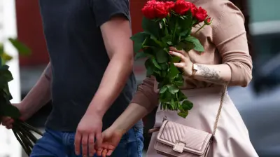 Kobieta i mężczyzna idą obok siebie trzymając bukiety róż