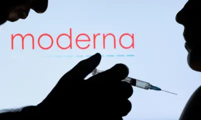 Bir kişiye aşı yapan bir adamın silüetinin arkasında moderna yazısı gözüküyor
