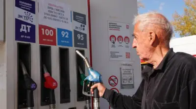 Автомобилист на автозаправке в Казани смотрит на надпись на колонке с бензином, держа в руках заправочный пистолет с АИ-92