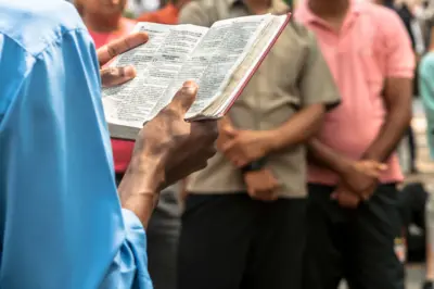 Pastor lendo a Bíblia, observado por pessoassites de apostas netellerpé atrás