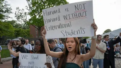Harvard Üniversitesi kampüsünde düzenlenen mitingde pankart tutan insanlar. Pankartlardan birinde 'Uluslararası öğrencilerin yanındayız' yazıyor.