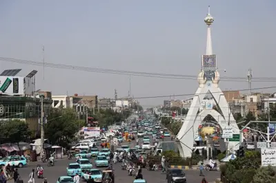 نمای از شهر هرات که در آن مردم و تردد موترهای تاکسی آبی رنگ دیده می‌شوند.