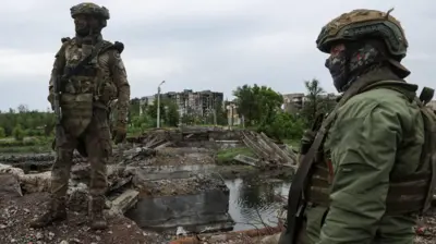Двое российских военных в камуфляже на фоне разгромленного города