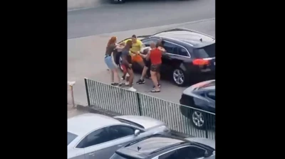 Zrzut ekranu z nagrania wideo przedstawiającego trzech mężczyzn atakujących mężczyznę i kobietę przed czarnym samochodem.