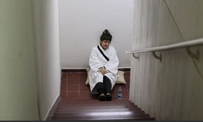 İsrail'de bir sığınakta merdivenlerin sonunda bir kadın tek başına oturmuş durumda. Yanında bir pet su şişesi var