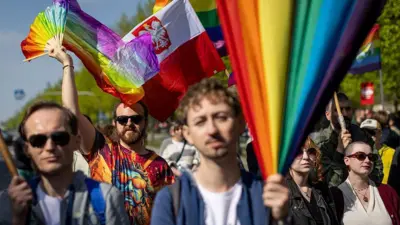 Kobiety i mężczyźni, podczas parady równości. Trzymają tęczowe flagi, na drugim planie widoczna jest również flaga Polski.