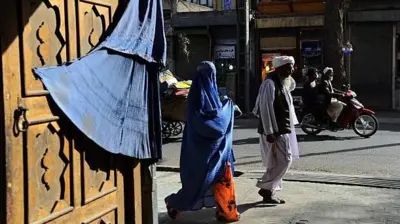 تصویر یک زن که با چادری که در کنار مردی در شهر هرات قدم می‌زند. 