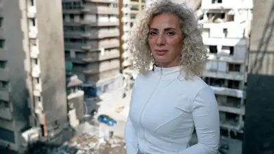 Bir kadın, bombalanmış bir alanı gören balkonda duruyor.