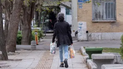 زنی در حالی که کیسه های خریدش را در دست دارد، در پیاده رو راه می رود