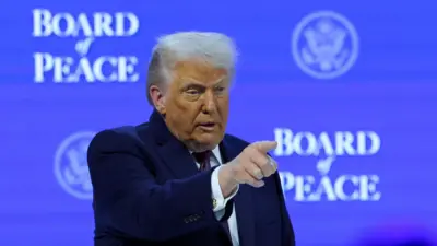 Donald Trump apontando para a plateia, sobre um fundo azul alusivo ao Conselho de Paz criado por ele